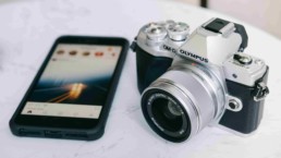 Telefon z włączonym ekranem i Instagramem oraz aparat marki Olympus na marmurowym stole